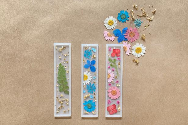 To make a DIY resin bookmark, first trim the flowers to fit the bookmark molds with scissors. Then add the flowers and bits of gold flake to the molds with tweezers.