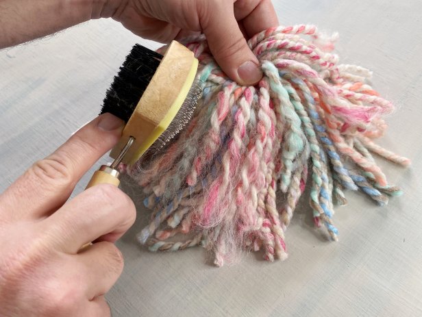 Cut the looped ends of the yarn bunch with a pair of scissors. Hold the beard in the center and shake it to cut any looped pieces of yarn that might have been missed. Use your fingers, brush or comb to carefully unravel the ends of the yarn for a fringe-like fluffy texture. Tip: Use an inexpensive clean pet grooming brush instead of buying a macrame brush or comb.