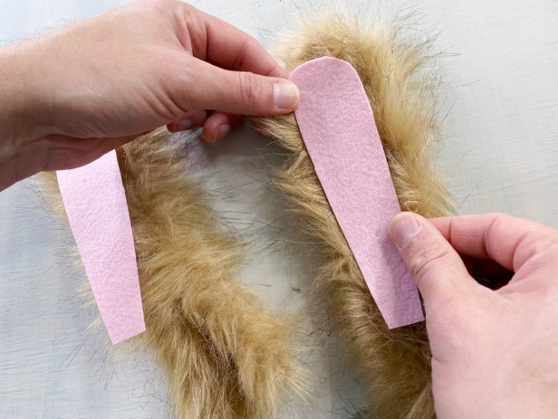 Measure and cut the fuzzy pipe cleaner into two 20’’ pieces. Bend them each in half and manipulate them to mimic the shape of bunny ears. Out of felt, cut two long, almond-like shapes for the inside of the ears. Use a glue gun to add a slight amount of hot glue around the edge of the felt. Then press the felt into the center of the pipe cleaner.