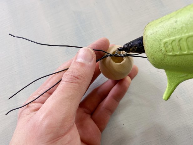 Cut three six inch pieces of wire. Hold them together and wrap them around each other in the center. Glue the center of the wire to the back of the wooden bead with hot glue. Lift the brim of the hat and carefully glue the bead directly above the beard slightly under the brim of the hat. Tip: If the brim of the hat does not stay over the nose, add a tiny amount of hot glue to the back of the brim to help it stay in place.