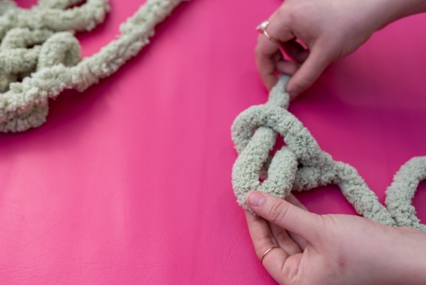 Roll out yarn and leave about 7’’ for the tail and put that to the side. Make the first loop. Fold the yarn over itself to make a loop, then push the extra yarn through the hole and tighten the loop into a knot. Tip: The tightened loop hole should allow about three fingers in width. Next, take the working yarn and put it through the loop to make another one; continue steps to create 15 total loops that make the chain.