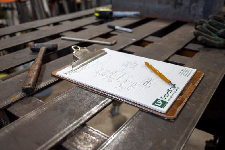 Furniture Dimensions on Clipboard Atop Steel Work Bench Near Hammer