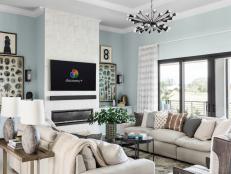 Soothing ocean tones bring a calm and tranquil feel to the living room at HGTV Smart Home 2021. Ample seating in front of the fireplace invites relaxation while natural light illuminates the room from the large glass doors that lead outside.