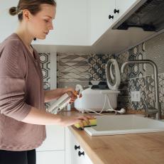Woman Wiping Sink With Sponge And Holding Spray Cleaner
