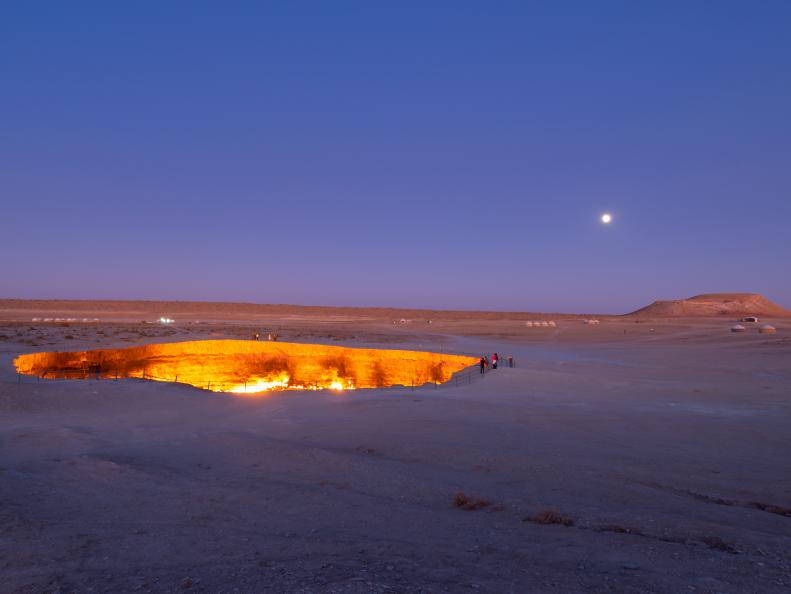 A glowing crater filled with gas in a sandy desert at twilight