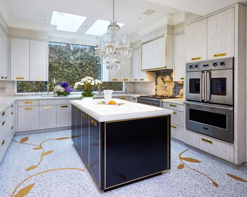 The trend for glamorous gold touches "resets the bar on the cold gray tones, stainless hardware and dull unlacquered brass fixtures that we’ve seen in recent years," accoreding to Joyce D. Silverman of Joyce D. Silverman Interiors. 

The look was achieved with the understated glimmer of bespoke hand-brushed gold ceruse oak cabinetry, contrasting gold trimmed high-gloss island, shining brushed brass hardware by P. E. Guerin, and elegant brushed brass plumbing fixtures. Tying it all together, a much-loved brushed brass pot-filler extends from the custom multi-color and gold floral tile mosaic behind the range, which adds a pop of pattern and color, including the homeowner’s favorite hue, indigo, to the kitchen. The gold infused theme is anchored by the custom mosaic tile floor inspired by the New York Plaza's famous food court - a sentimental destination for the travel loving owners - that elegantly flows through the kitchen and breakfast room beyond.
