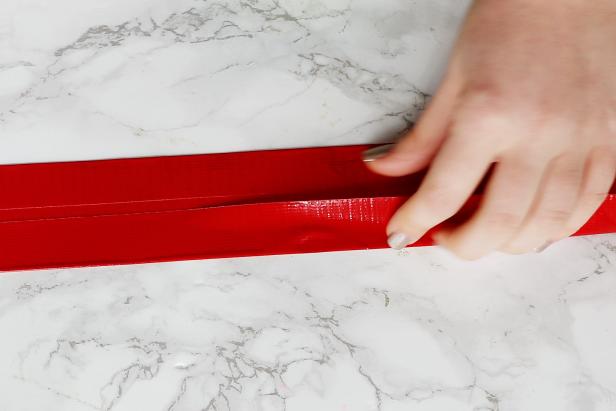 Cut a strip of duct tape and cover the sticky side with two additional strips. Fold them over the edge to get a long strip of tape with all of the sticky sides covered up. Make one that is 11¼”, three that are 22½”, and three that are 25”.