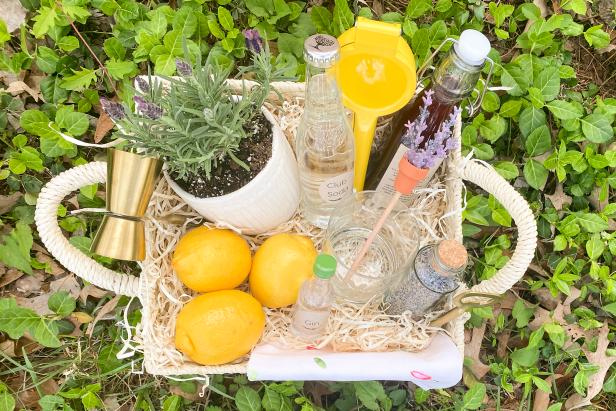 To make Danielle's Mother's Day cocktail gift basket you will need, a basket, crinkle paper, a small potted plant, barware accessories, DIY cocktail mix, club soda, a crafty stirrer, dried lavender, fresh lemons and a lemon squeeze.
