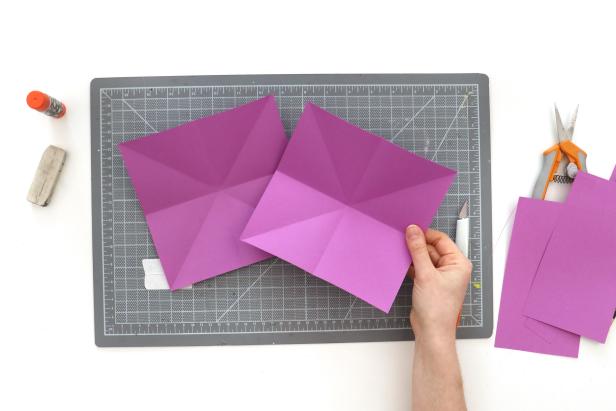 Cut two pieces of colored paper into 7” squares. Your paper should be the weight of printer paper, rather than card stock. Fold them in half diagonally, horizontally, and vertically.