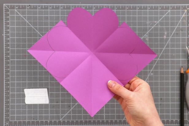 Cut and fold a piece of scrap paper the same way. Draw and cut out a curve from the corner of the paper that creates a heart when the paper is opened. You may make a few attempts on scrap paper until you get a heart shape you’re happy with. Once you have your pattern, trace it onto the colored paper and cut it out.