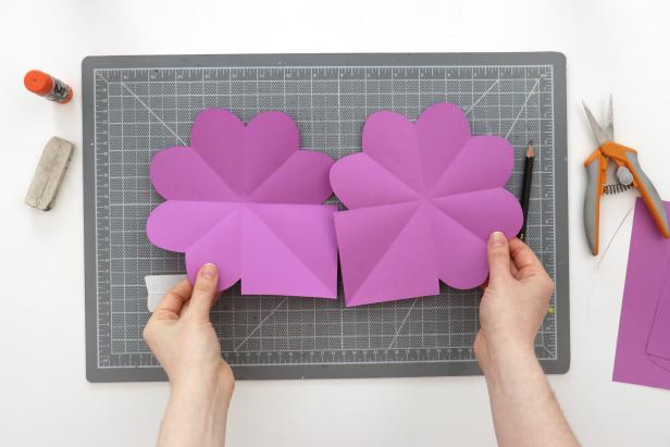 Fold the page horizontally and vertically to trace the heart onto those quadrants. Cut them out to end up with three hearts and one square on each sheet. Repeat this for the second piece of paper and glue them together with the squares overlapping.