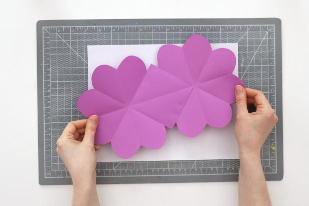 Fold the page horizontally and vertically to trace the heart onto those quadrants. Cut them out to end up with three hearts and one square on each sheet. Repeat this for the second piece of paper and glue them together with the squares overlapping.