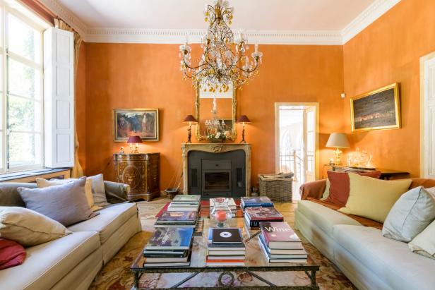 A classic crystal chandelier hangs in the center of this traditional orange drawing room. Two matching cream sofas lined with throw pillows provide cozy seating for the space, while a plethora of coffee table books serve dual purposes as entertainment and decor.