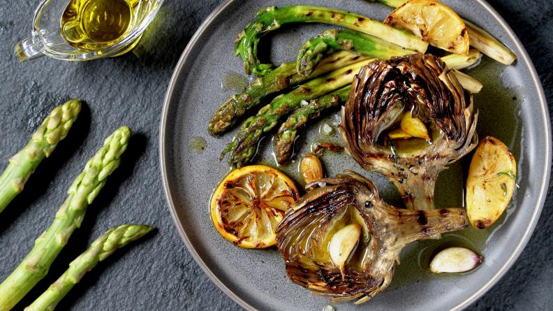 Grilled artichokes and asparagus on a plate with lemons