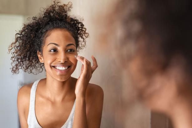 A Black woman applies skincare product to her face