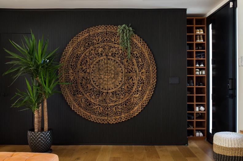 Black wall with large circular wooden carving and tropical plants.