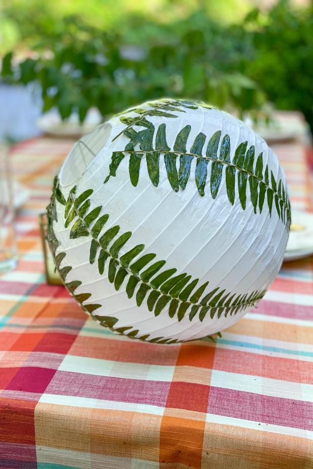 HGTV Handmade’s Danielle Boaz makes a pressed fern paper lantern for summer. To make your own, you will need 10’’ white hanging paper lanterns, LED mini lights, a low-temp hot glue gun, decoupage glue, pressed fern sprigs, a foam brush and scissors.