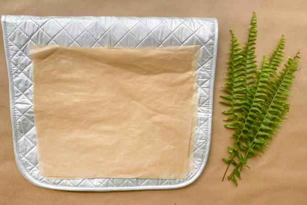 Prepare the ferns for pressing by placing two pieces of parchment paper on an ironing mat.