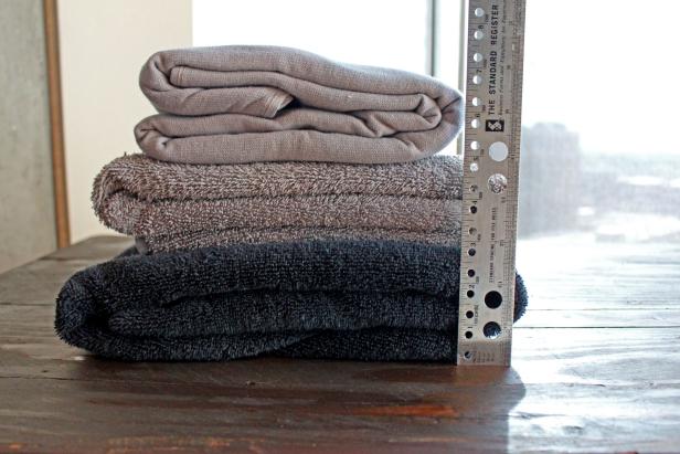 A stack of three towels on a table with a ruler measuring thickness.