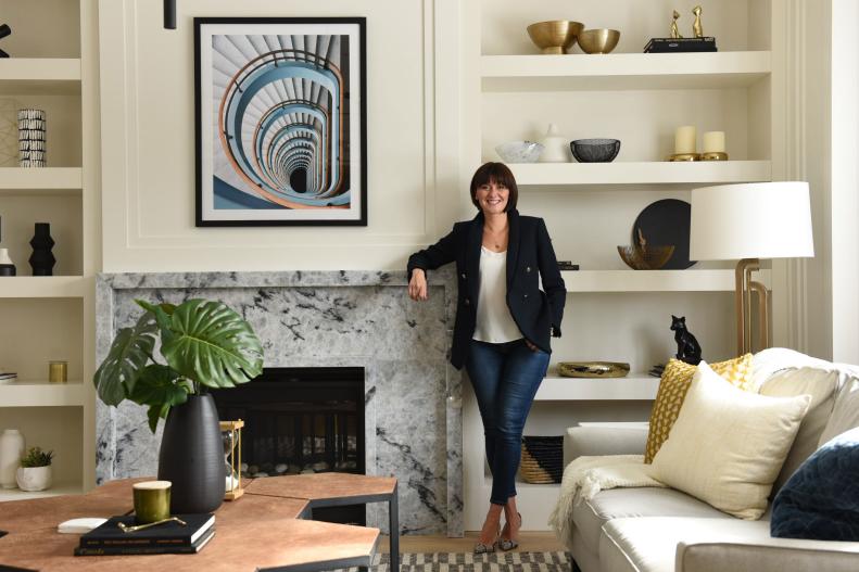 Designer Rebecca Hay stands in front of living room fireplace.