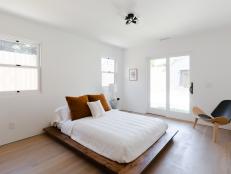 A low platform bed with white sheets in a minimalist, sunny room