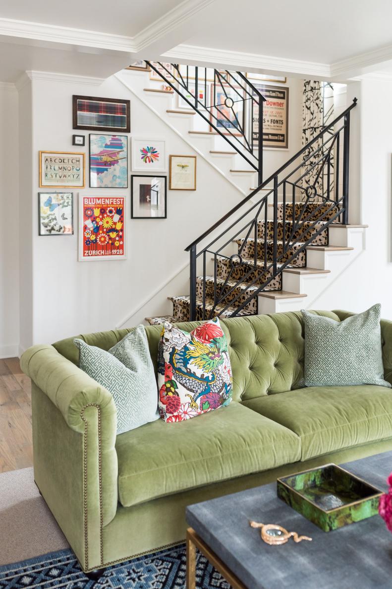 Moss green tufted sofa before stairs with iron rail and framed art.