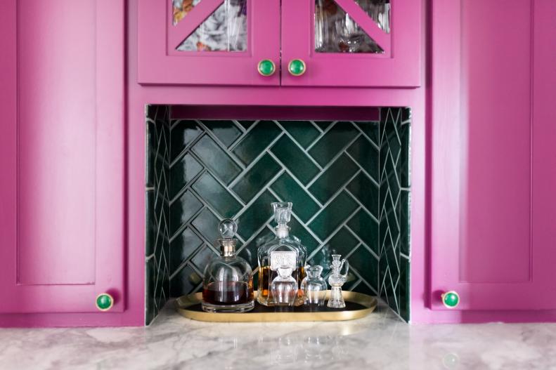 Bright pink cabinets frame a green tiled bar nook on a marble counter.