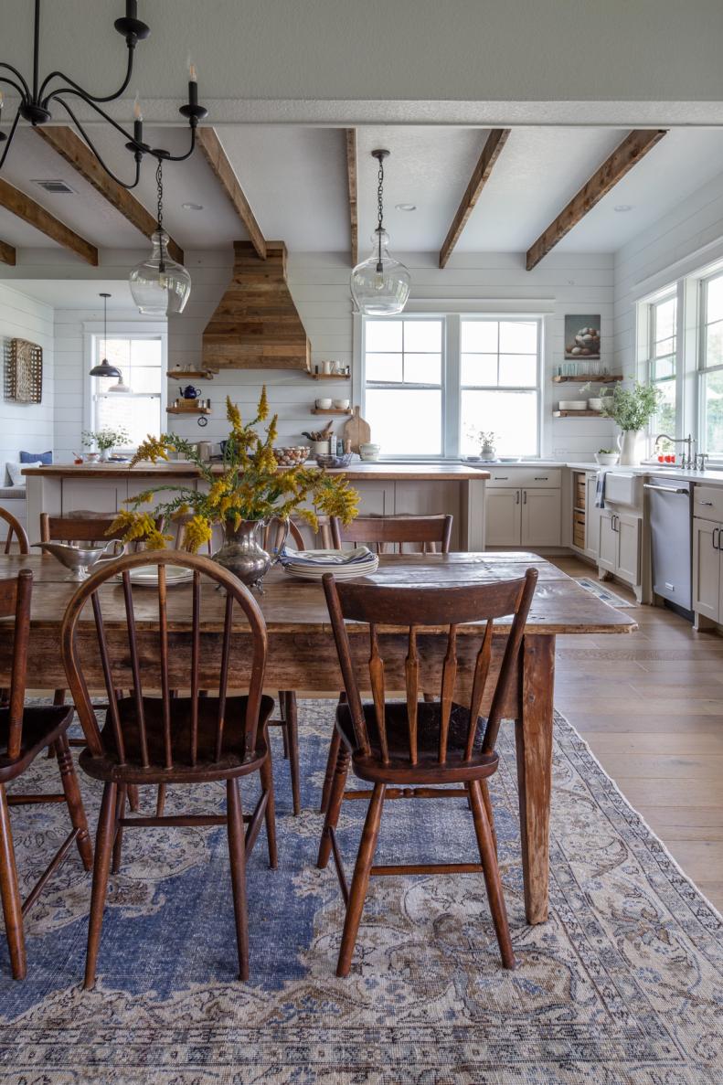 Antique wood chairs and table on a blue rug in an open kitchen.