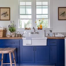 Rustic Laundry Room With Farmhouse Sink, Bold Blue Cabinets and Bird Lithographs