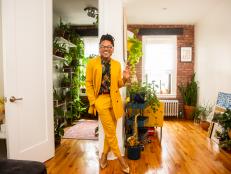 Person in bright yellow suit smiles in apartment filled with plants
