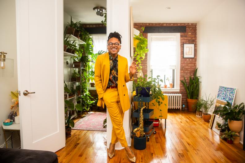 Person in bright yellow suit smiles in apartment filled with plants