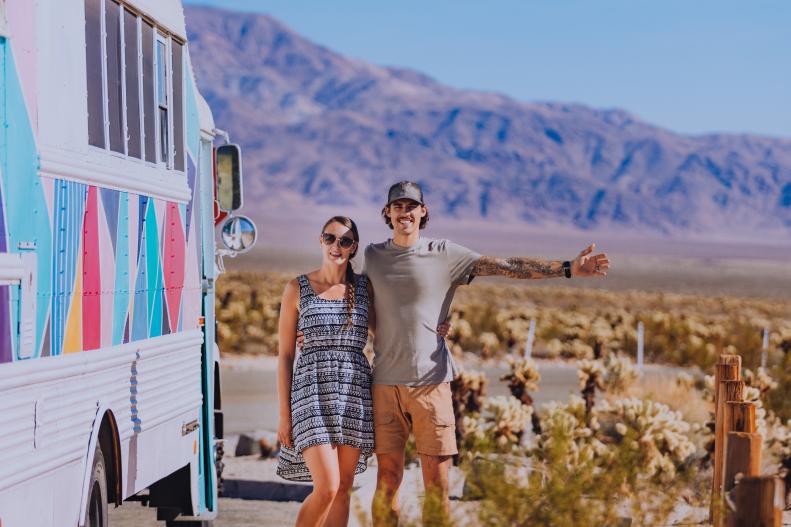 Couple Stands Beside Colorful Bus Home in Desert Smiling to Camera