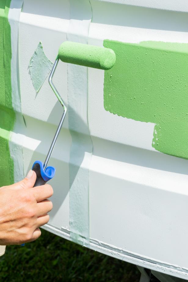 Next, pour green exterior paint into a paint tray and dip a roller into the paint. Add the first coat to the designated stripe sections and wait until dry. Then, add a second coat for a bolder look. Once dry, carefully peel off the painter’s tape to reveal perfect green stripes.