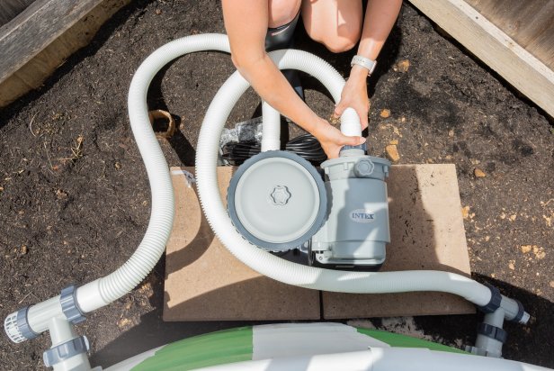 Team lift the painted stock tank pool and place it onto the sandy circle. Then hook up the ground plunger valves, above ground pool pump and filter per their instructions. Then, check for water leaks by spraying water from a hose directly onto the drain ports to see if water leaks from the other side. Next, climb into the tank and use a small vacuum to remove any debris or shaved metal from the inside. Wipe down the inside with a rag and white vinegar to prepare for filling. Place a water hose inside the tank and fill until full.