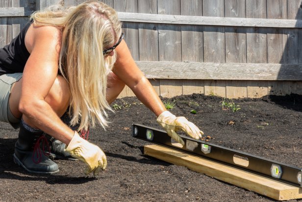 Before you begin, ensure the backyard area where the stock tank pool will live is perfectly level. If your yard is not level, build a raised bed following these steps. Stake out the dimensions with a string and rebar. Then, dig small trenches along three sides of the uneven side or slope. Measure the wood to fit the trenches and dig holes for posts. Mix concrete, set posts and let set for one hour. Last, screw the boards to posts, fill the area with dirt and tamp to level. Check accuracy with a level.