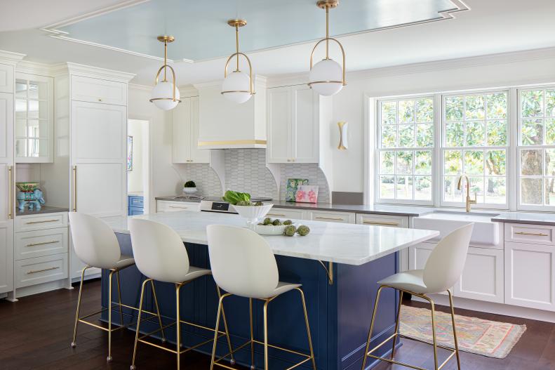 White kitchen with a blue island and large windows.