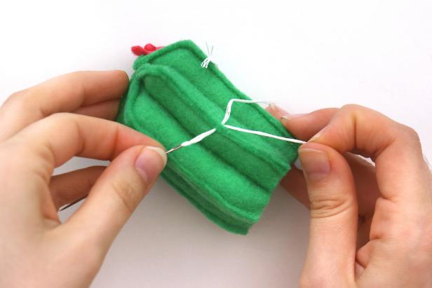 Cut small pieces of white embroidery thread and use an embroidery needle to thread them through the cactus. Tie a double knot and trim the ends to get a cactus “spike.” Add these randomly all over the cactus.