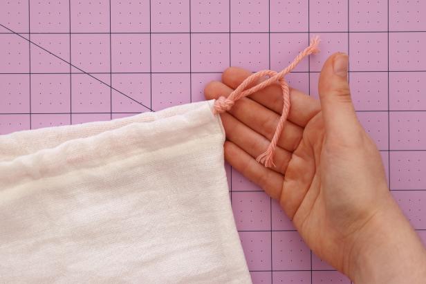 Push one piece of string through a large safety pin and feed it all the way around the bag. Tie the ends in a knot. Repeat with the other piece of string, starting and ending on the other side.