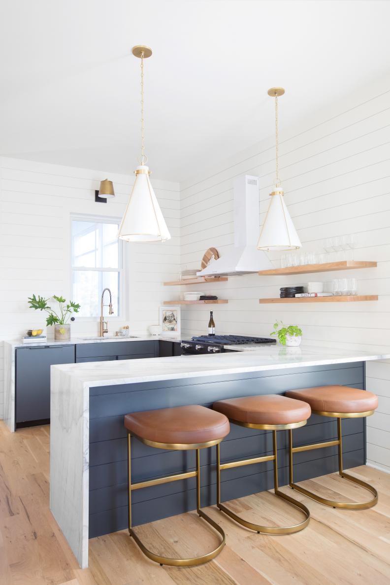 Three brown stools at dark peninsula in white kitchen with pendants.