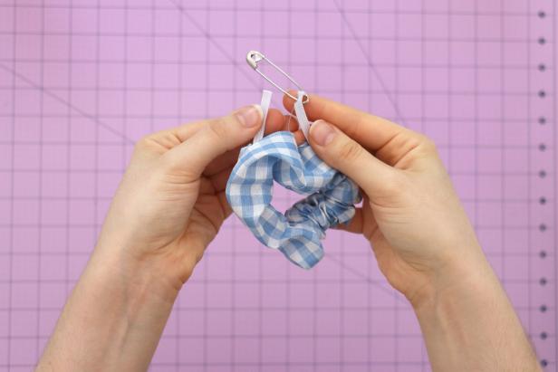 Cut an 8” piece of elastic. Add a safety pin to the end and feed it through the scrunchie. Hand sew the ends of the elastic together. These stitches can be messy and uneven, since it will be hidden inside the scrunchie.