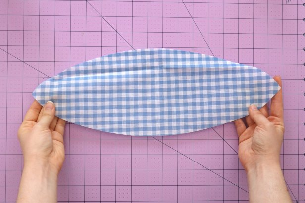 To make the scarf, fold your fabric twice so you have four layers. Cut a long curve between the folded edges. This curved piece should measure around 8” x 1.5.” Unfold it to get a long oval that measures around 16” x 3.” Fold it in half lengthwise with the right sides together and press it with an iron.