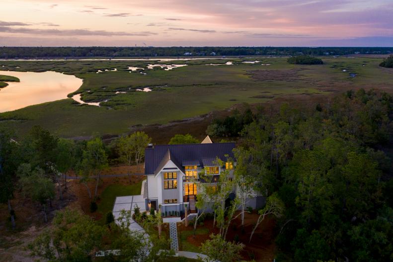 Large white mansion on wooded hill above river and sunset.