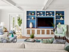 White living room with blue-backed built-in shelving around TV.