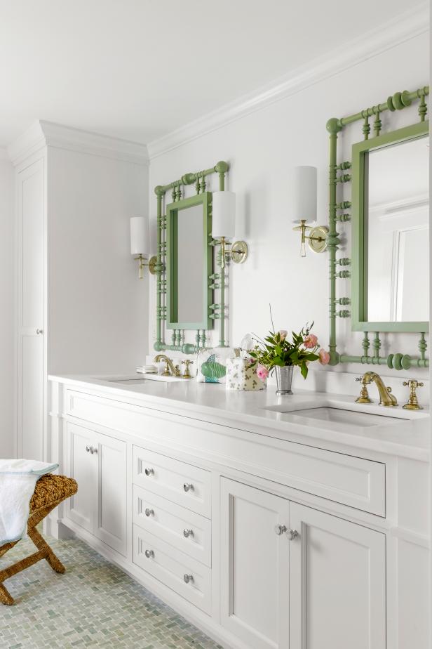 White bathroom with two intricate green mirrors and two sinks. 