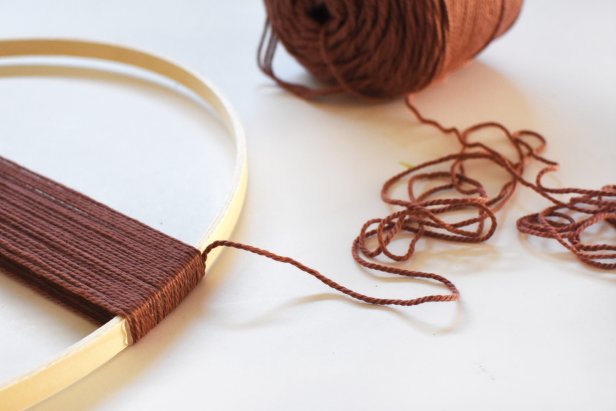 Yarn is wrapped around an embroidery hoop and hot glued in place as part of a yarn art ring project.