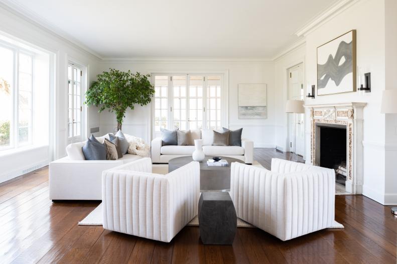White room with dark floors, square chairs and ornate fireplace.