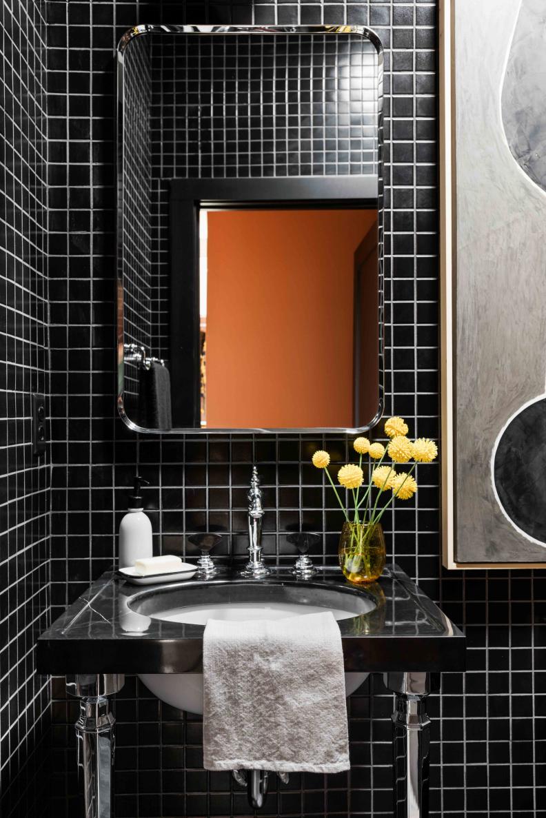 A modern industrial vanity with black marble counter and linear chrome legs compliment elegant black tile in this polished, impressive guest bathroom.