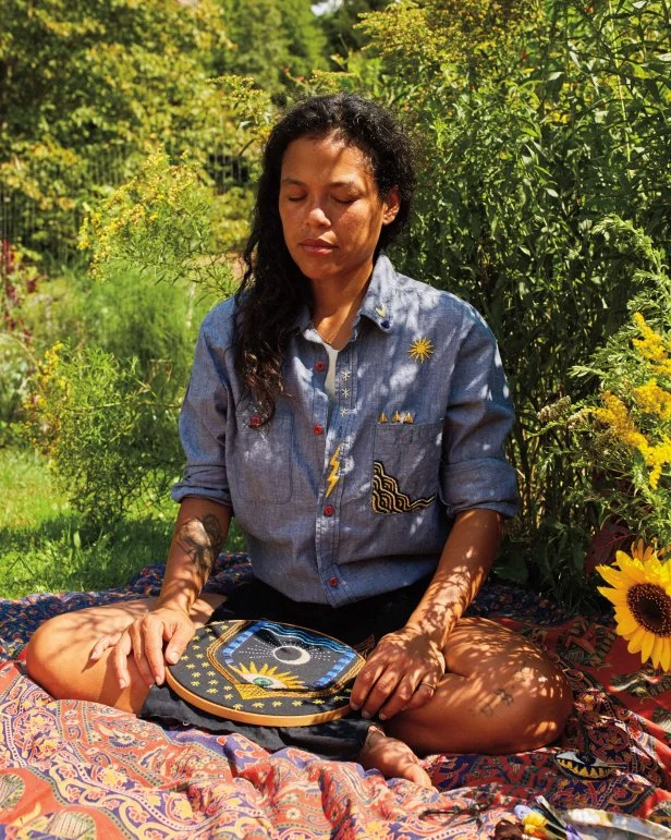 Woman Wearing Embroidered Clothing Sits On Grass In Quiet Meditation