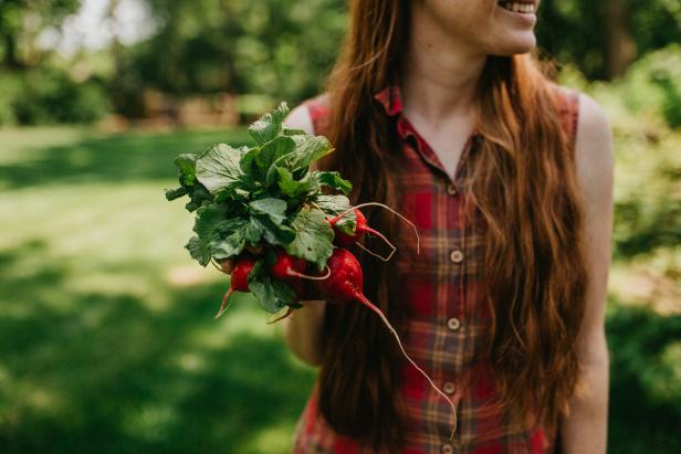 A woman holding a handful of just-picked radishes with long roots and green tops.