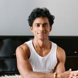 拉吉夫·苏伦德拉（Rajiv Surendra）姿势，在钢琴附近为摄像机微笑